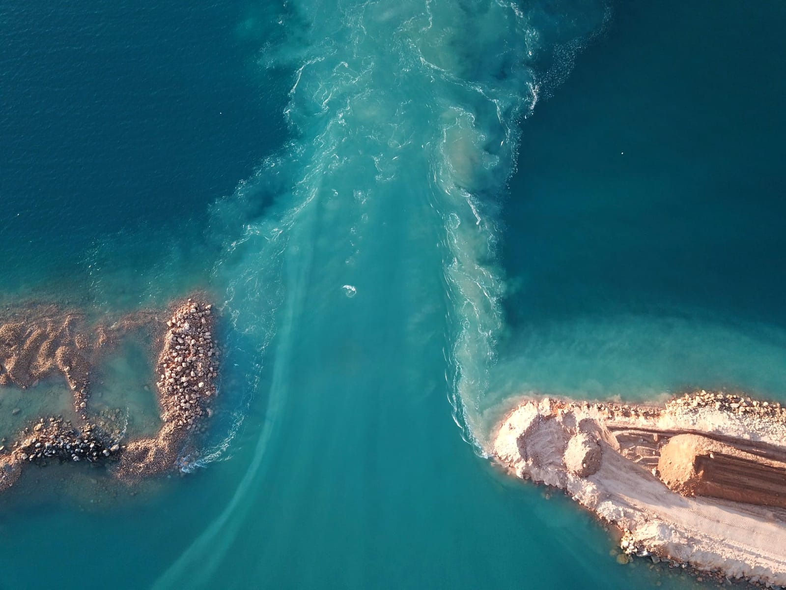 Aerial photograph looking straight down at a breach between two rock armoured headlands at Useless Loop, with turquoise water and sediment pouring through the gap