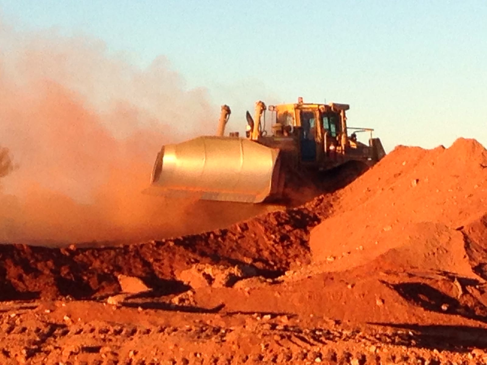 A CAT wheel loader pushing a bucket of red gravel through its own dust cloud on a Mid West job